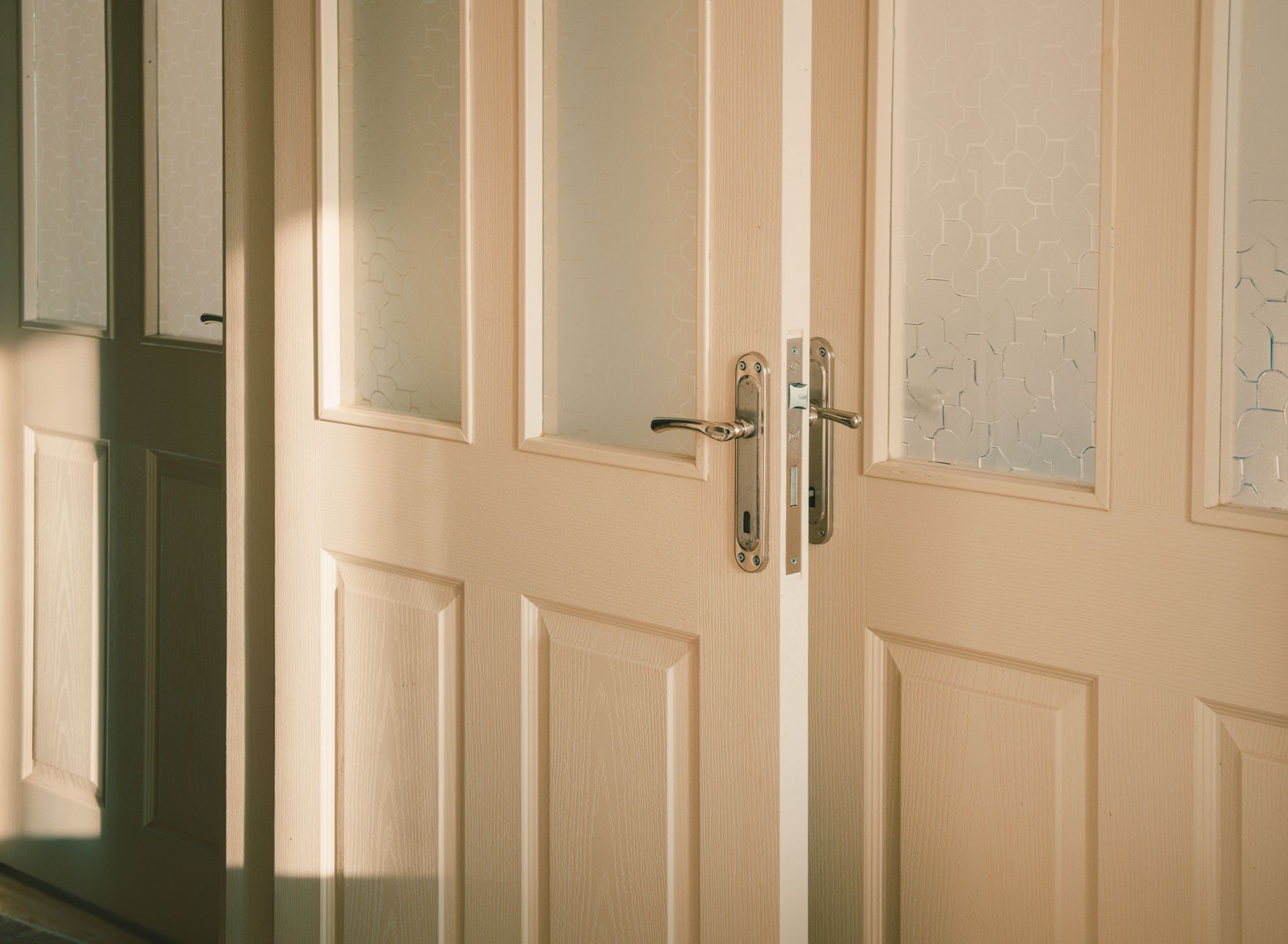 Elegant wooden doors with frosted glass panels softly illuminated by streaming sunlight.